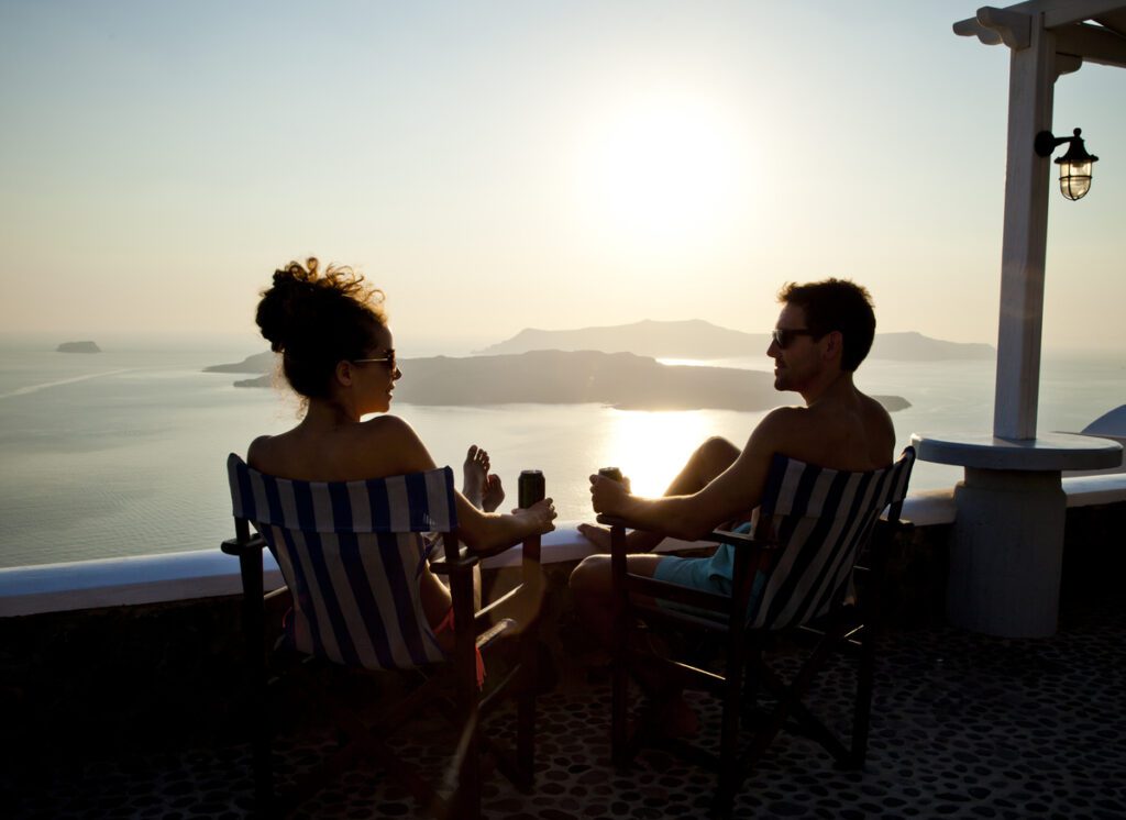 Silhouette of a young couple enjoying a sunset with a drink. Santorini, Greece.
