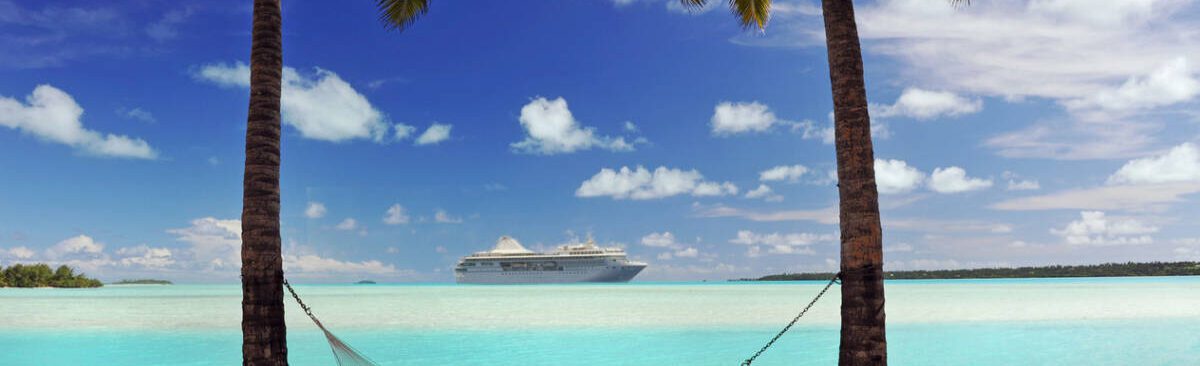 A cruise ship passes an idyllic tropical island in the South Pacific with hammock and palm trees in semi-silhouette