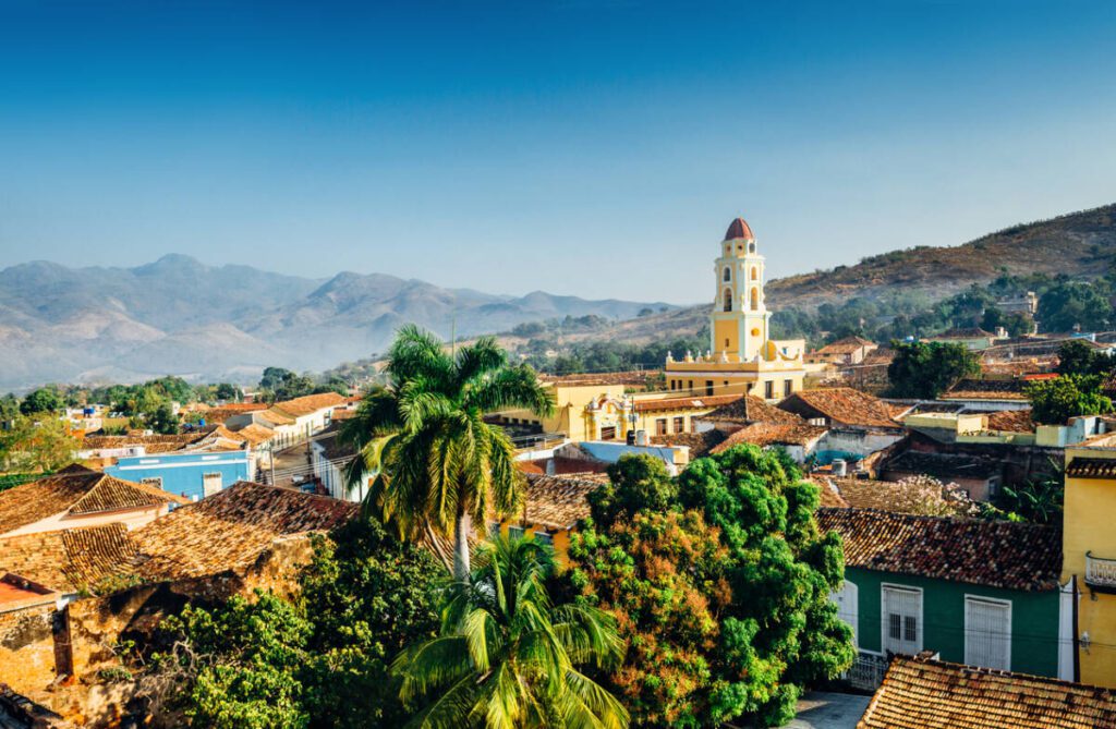 Panoramic view over the city of Trinidad, Cuba with mountains in the background and a blue sky. The bell tower belongs to the Iglesia y Convento de San Francisco.