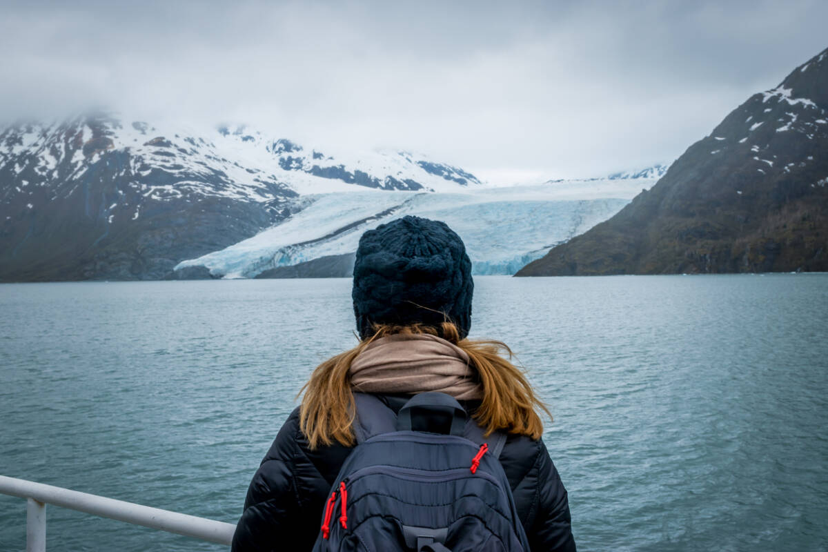 Woman doing a cruise and looking at the Portage glacier in Alaska with snowcapped mountains in background.
